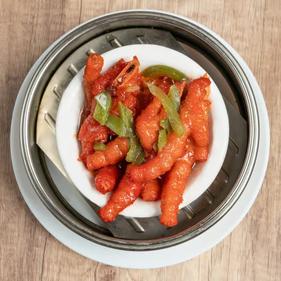 Red chicken feet with green peppers in a white bowl, inside a metal steamer basket.
