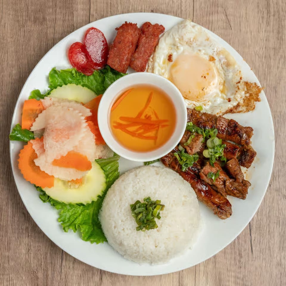 Vietnamese grilled pork, fried egg, rice, pickled vegetables, and dipping sauce on a white plate.