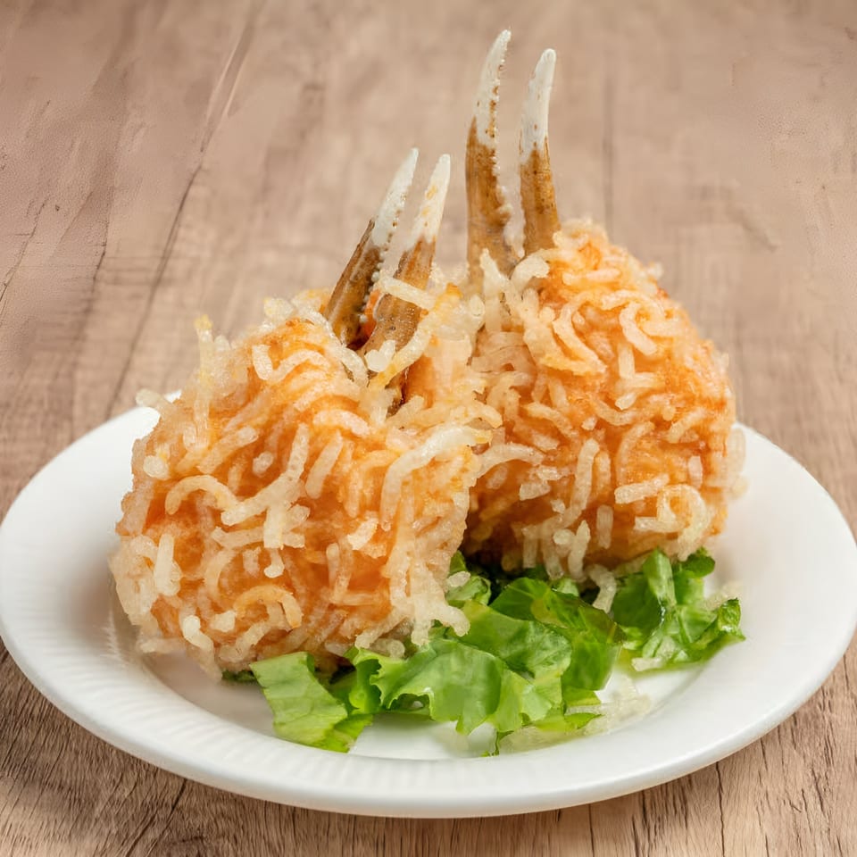 Two crispy fried crab claws with shredded potato coating, served on a white plate with lettuce.